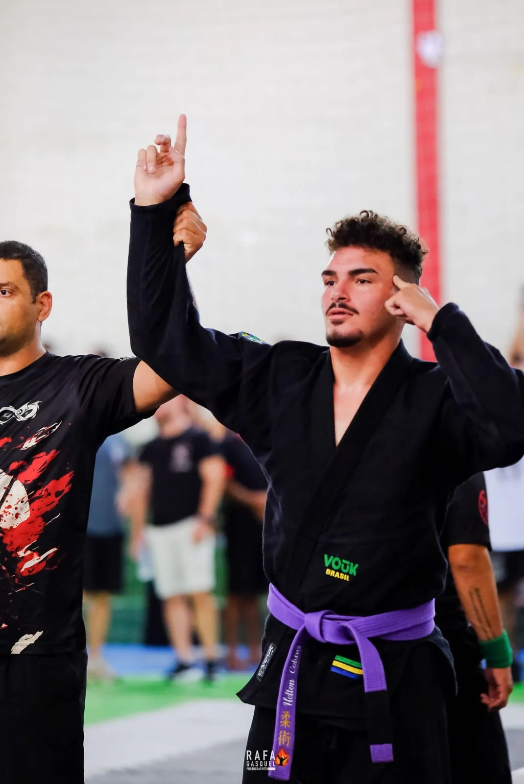 Professor Helton Colares de kimono e faixa roxa, com o braço erguido em uma competição